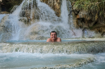 Fototapeta na wymiar Young man bathes in the healing thermal mineral springs in the resort of Saturnia Italy