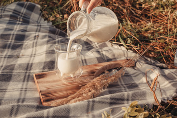 A woman pours milk from a decanter into a glass. Checkered plaid and wheat. Hands close up
