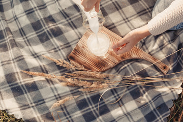 A woman pours milk from a decanter into a glass. Checkered plaid and wheat. Hands close up