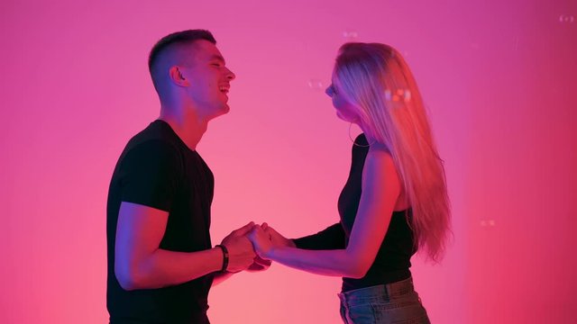 Young couple holding hands looking to each other. Carefree free lovers laughing and smiling in neon vivid light with red and blue colors