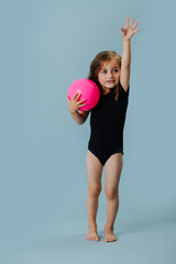 Little girl in a black leotard with pink gymnastic ball over blue background