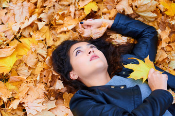 woman lying with autumn leaves in city park, outdoor portrait