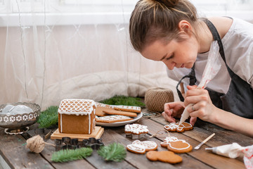 Icing of Christmas bakery. Woman decorating honey gingerbread cookies on wooden brown table....