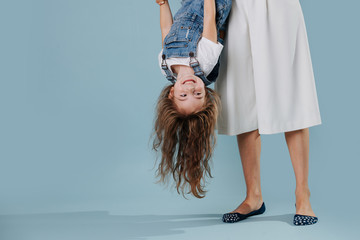 Mother is holding her laughing daughter upside down over blue background