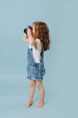 Little girl is taking an image with a vintage mirrored camera over blue.