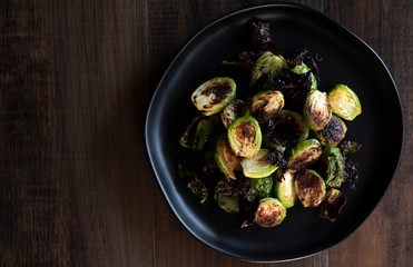 crispy baked brussel sprouts drizzled with sauces on a black plate on dark wooden table