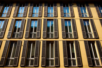 Close up. Symmetrical windows with wooden shutters in an Italian traditional building in the center of Milan, Lombardy, Italy. European modern architecture. Street view of the building facade.