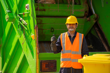 Garbage removal worker in protective clothing working for a public utility emptying trash container.