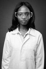 Young beautiful African Zulu woman doctor wearing protective glasses against brown background