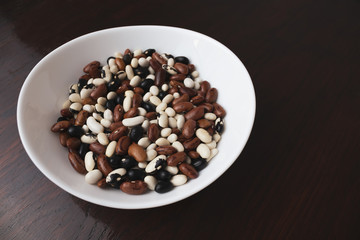 Beans in a white plate on a brown background. Beans of different colors on the table. Healthy eating