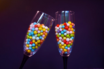 Two clinking Champagne glasses filled with small colorfull foam balls on dark black background, fun concept for birthday party or new year event celebrations
