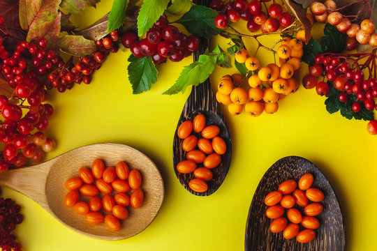 Vitamin coenzyme Q10 pills on a spoon. Yellow background with berries. Seasonal beriberi