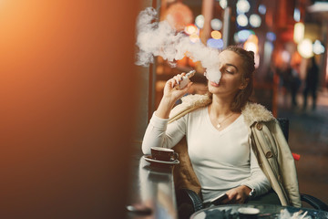 girl drinking coffee and using her phone outside a cafe during the evening