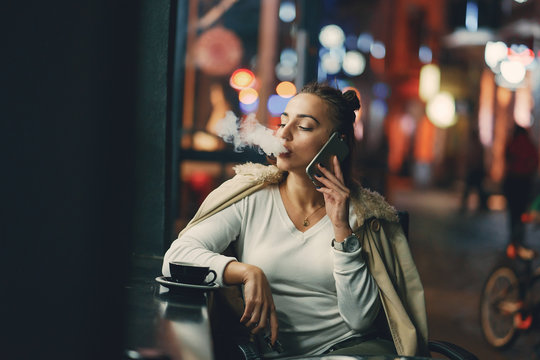 girl drinking coffee and using her phone outside a cafe during the evening