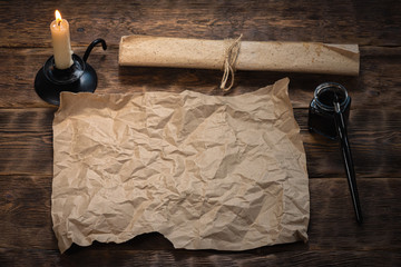 Blank paper parchment with copy space, quill pen and burning candle on wooden desk background. Treasure map mockup.