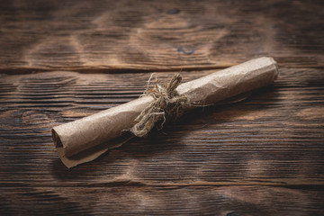 Old parchment letter wrapped by rope on brown wooden desk background.