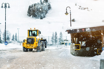 Big loader machine with steel metal chains removing big snow pile from city street at alpine...