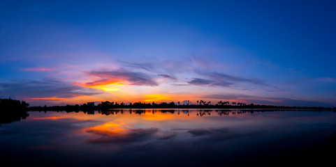 Panorama silhouette tree in asia with sunset.Tree silhouetted against a setting sun.Dark tree on open field dramatic sunrise and reflection in water. 