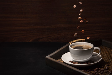 scatteing coffee beand on coffee cup with coffee beans on bamboo tray on wooden background