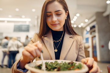 Girl eats vegetable salad. Lady sitting in a cafe. Brunette in a brown coat