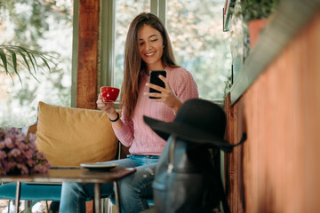 Happy hipster woman in retro cafe. A young girl use a mobile in a cafe while drinking coffee.