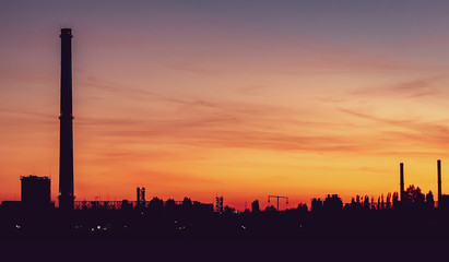 Sunset in the industrial zone. A factory with a tall chimney and glowing towers. Beautiful sky with clouds.