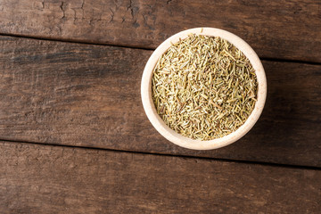Dried rosemary leaves in bowl on wooden table. Close up. Top view