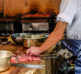 Japanese chef cook Unagi or eel being grilled , many pot and kitchenware on wooden table, chef prepared skewered raw fresh stick eel seafood (Unagi) before girll in  restaurant ,Japan