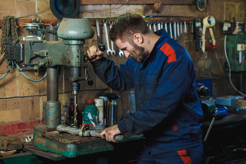 A mechanic drills a detail on a drill press. Workflow mechanic in a car garage. Auto service concept.