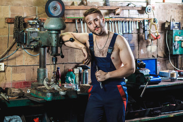A mechanic in a blue protective suit is standing in a car garage near a drill press. Auto service concept.