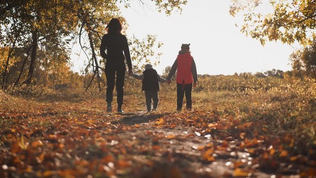 Mother and two children walking in the park and enjoying the beautiful autumn nature. Happy family on autumn walk.