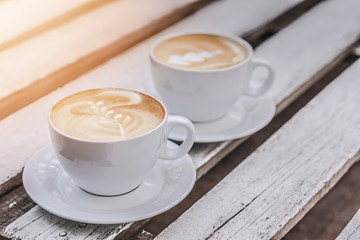 Two white big cups of coffee with art on white wooden table with copy space.