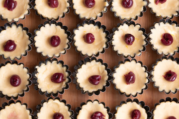 Small tarts with cherry and whipped egg whites and pistachio filling in metal forms before baking showing the process5