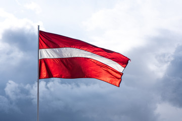 Latvian flag on the mast waving on the wind in the blue sky