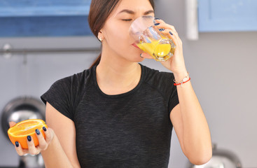 Sport Asian woman in a black t-shirt makes and drinks orange juice in the kitchen.