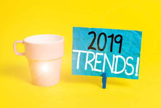 Handwriting text 2019 Trends. Conceptual photo general direction in which something is developing or changing Cup empty paper blue clothespin rectangle shaped reminder yellow office