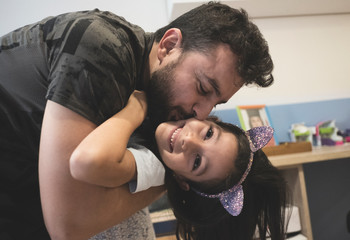 Father hugs and kisses daughter in everyday scene