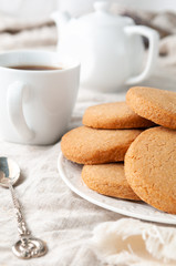 Round homemade shortbread cookies. In a white plate. On a linen tablecloth of gray color. In the background is a stack of cookies. White teapot and mug.