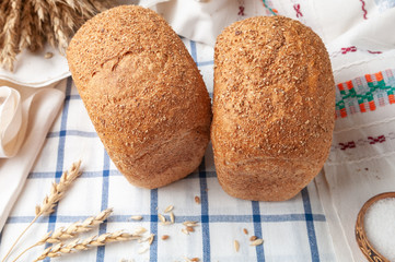 Two loaves of bran bread. On a white blue striped tablecloth. On the tablecloth ears of wheat and grain. View from above. Country style.