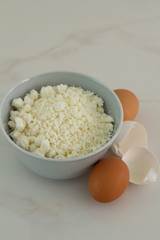 cottage cheese in a cup and chicken eggs on a white background