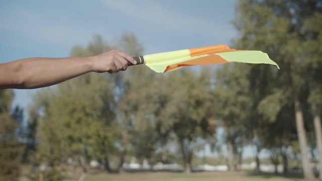 Close-up of raised flag for offside of assistant referee during soccer game over colorful natural background. Linesman hand with flag signalling for offside trap to referee during football match.
