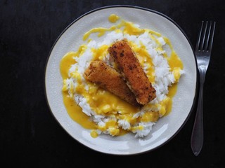 Rice with fish fingers and curry sauce on black background