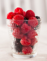 handful of fresh raspberry and blackberry berries in glass on white background