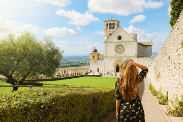 Tourism in Italy. Back view of beautiful girl enjoying view of the Basilica of Saint Francis of Assisi in Umbria, Italy. - obrazy, fototapety, plakaty