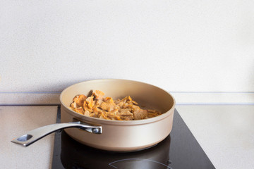 Chanterelle mushrooms preparing in the frying pan on the black stove. Cooking process, recipe concept. Close-up, copy space