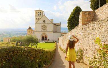 Tourism in Italy. Back view of beautiful girl walking towards the Basilica of Saint Francis of Assisi in Umbria, Italy. - obrazy, fototapety, plakaty