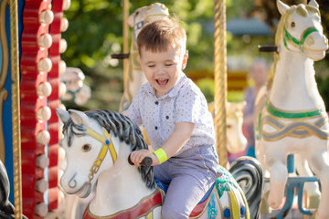 Blonde boy  riding colorful horse in the merry-go-round carousel in the entertainment park