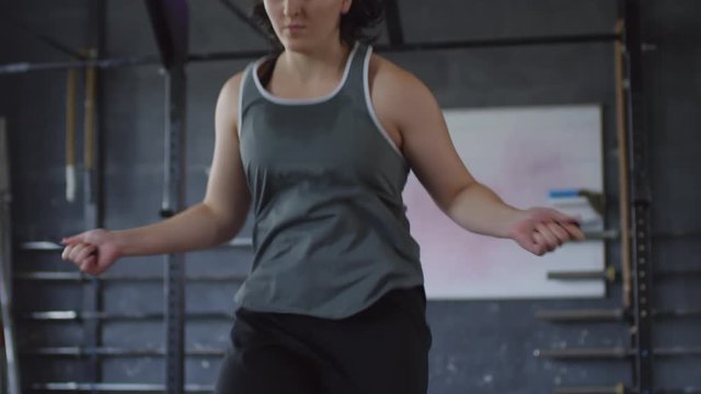 Tilt down slow motion shot of young female boxer performing high knee steps with jumping rope while exercising in gym
