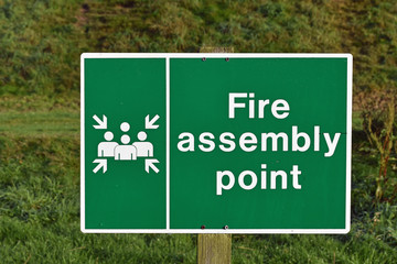 Fire assembly point sign with blurred grass background