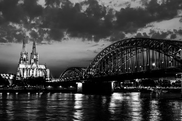 Beautiful black and white night landscape of the Cologne, Germany with gothic cathedral, railway and pedestrian Hohenzollern Bridge and reflections over the River Rhine